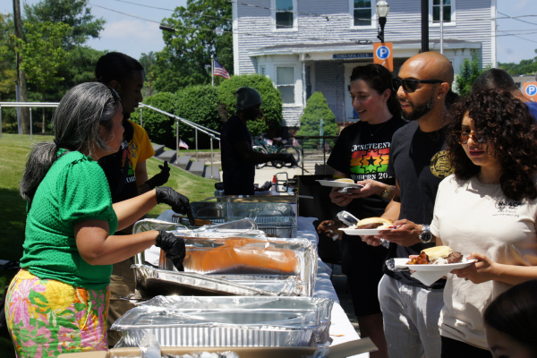 Volunteers and staff serving free hamburgers, hot dogs, and Caribbean food to attendees at Woburn Juneteenth 2025.