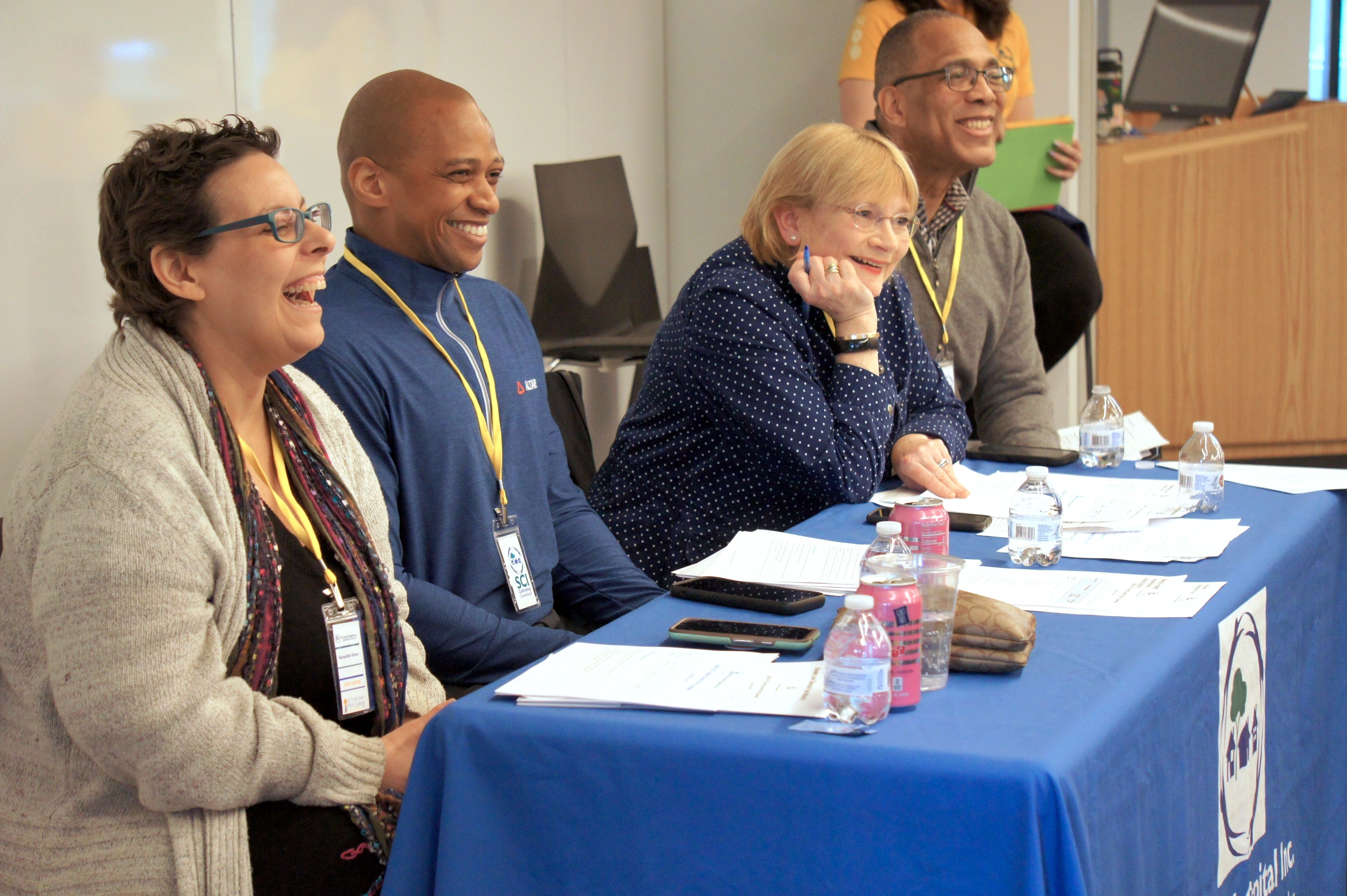 Four SCI Pitch Judges joyfully laughing together during a youth team presentation.